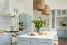 a beautiful coastal kitchen in light blue and white, with a mosaic tile backsplash, wicker lampshades and rattan stools plus greenery