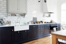 a beautiful kitchen with navy lower cabinets, a grey upper cabinet, a white hood, white subway tiles on the wall