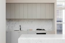 a beautiful minimalist kitchen with dove grey shiplap cabinets, a white marble backsplash and a matching kitchen island