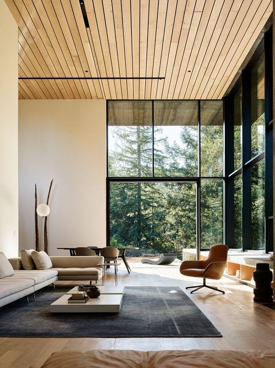 a biophilic living room with glazed walls to maximize the views and natural light and a wooden ceiling and floor