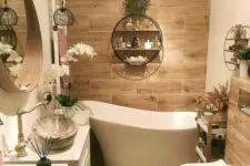 a boho bathroom with large scale wood tiles, a bathtub, a white vanity, some blooms and greenery and a toilet
