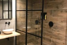 a bold contemporary bathroom with wood look tiles, a wooden vanity and black framing for a dramatic touch