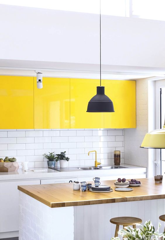a bold contemporary kitchen done in white, with bright yellow upper cabinets, a wooden countertop and a white subway tile backsplash