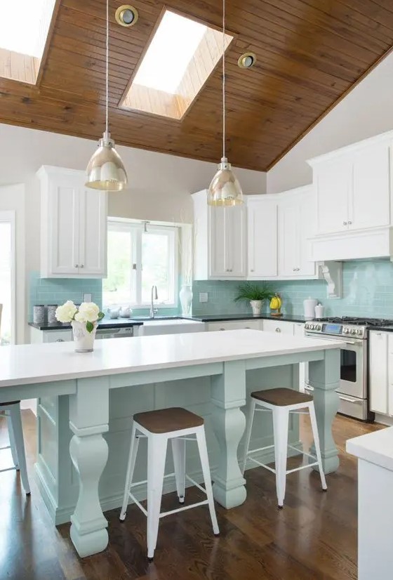 a bright beach kitchen with an aqua kitchen island and aqua tiles, white shaker cabinets, glass pendant lamps and vintage stools