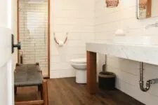 a catchy bathroom with shiplap walls and a rich-stained wood tile floor, a shower space, a long vanity and a unique lamp