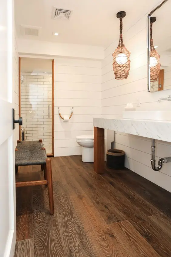 A catchy bathroom with shiplap walls and a rich stained wood tile floor, a shower space, a long vanity and a unique lamp