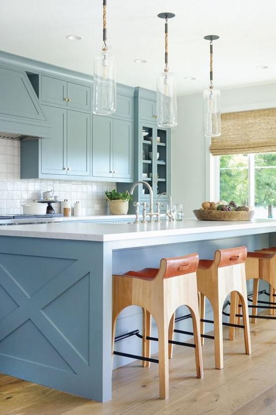 a chic coastal space with light blue cabinets, a blue kitchen island, glass pendant lamps and wood and leather stools