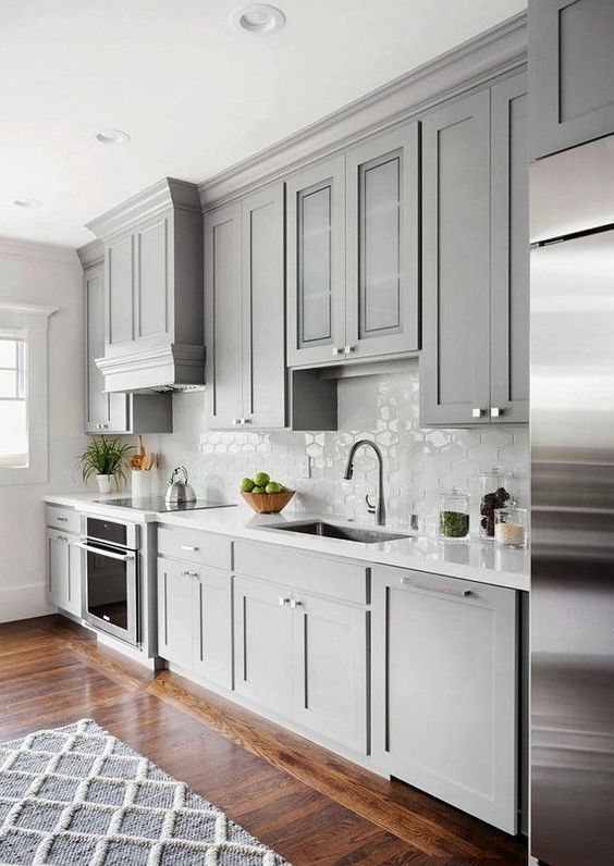 a chic contemporary dove grey kitchen with a white tile backsplash and countertops plus a rich stained floor