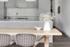 a chic kitchen with grey shaker cabinets, a white subway tile backsplash, white pendant lamps, a stained table and metal wire chairs