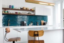 a chic kitchen with sleek white cabinets, a bold blue tile backsplash, a kitchen island, stained stools and shelves
