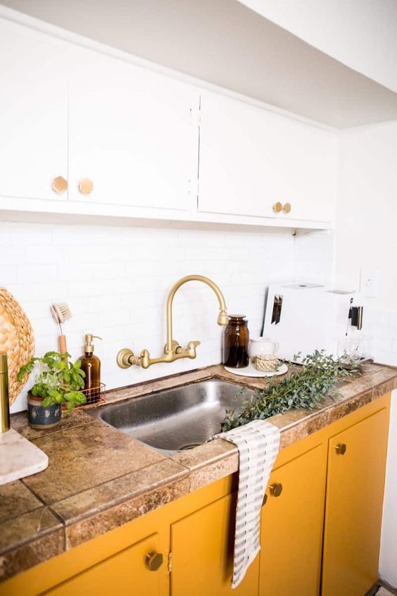 a chic kitchen with white upper cabinets and buttercream lower ones plus a stone countertop and brass touches looks cool