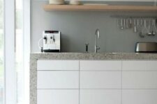 a chic minimalist kitchen with sleek white cabinets, a concrete backsplash and grey stone countertops plus a wooden shelf