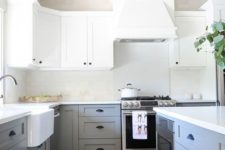 a chic two tone kitchen with white upper cabinets and light grey lower ones, black handles and dark wooden beams