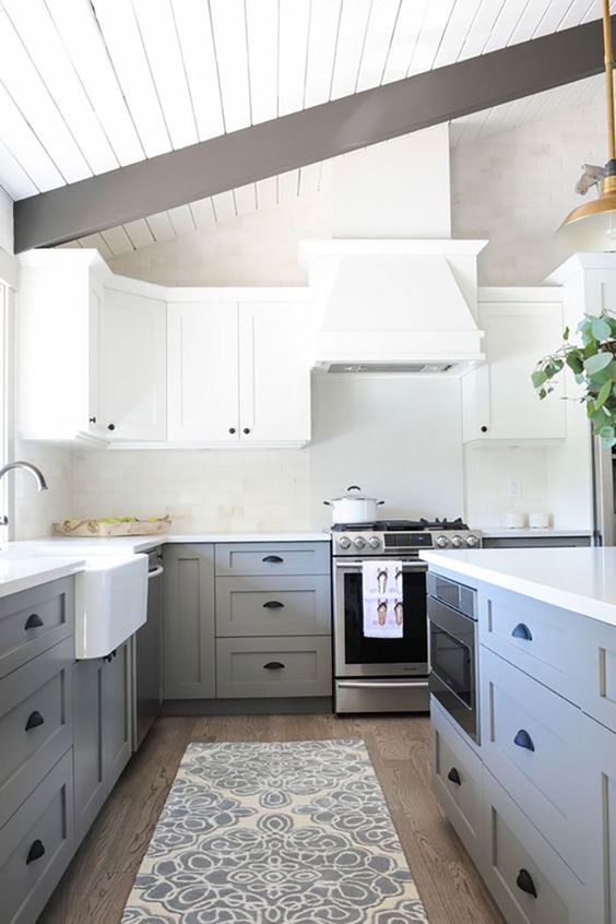 a chic two tone kitchen with white upper cabinets and light grey lower ones, black handles and dark wooden beams