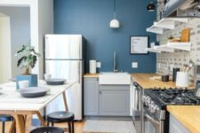 a cihc and cool kitchen with a navy accent wall, grey cabinets, butcherblock countertops, a trestle table and black stools