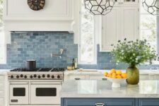 a classic sea-inspired kitchen with white shaker cabinets, a blue tile backsplash, a blue kitchen island with white stone countertops and beautiful faceted lamps