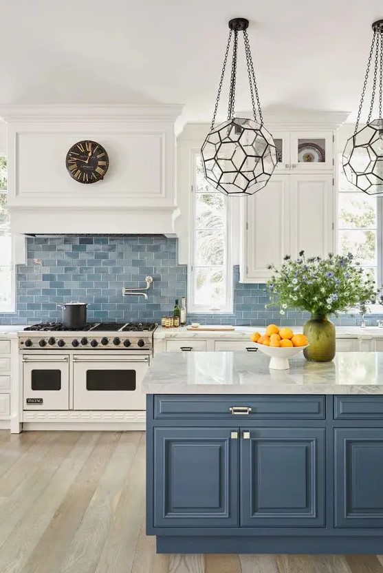 A classic sea inspired kitchen with white shaker cabinets, a blue tile backsplash, a blue kitchen island with white stone countertops and beautiful faceted lamps