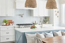a coastal cottage kitchen with white shaker cabinets and a glossy tile backsplash, a blue kitchen island with a seating space and woven pendant lamps
