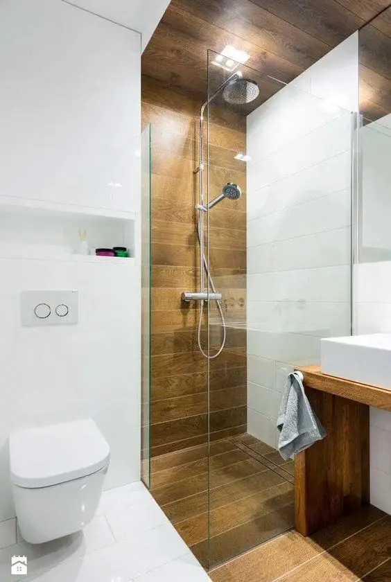 A contemporary bathroom with white and wood inspired tiles, a vanity, a shower and a mirror plus built in lights