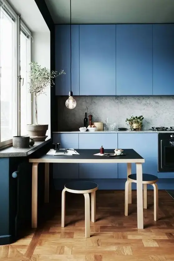 a contemporary blue kitchen with a grey stone backsplash and countertops, a black and stained table and stools