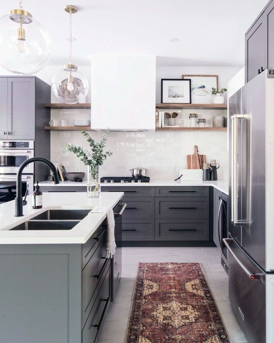 a contemporary kitchen with grey cabinets, a white hood and tile backsplash and white countertops plus a boho rug