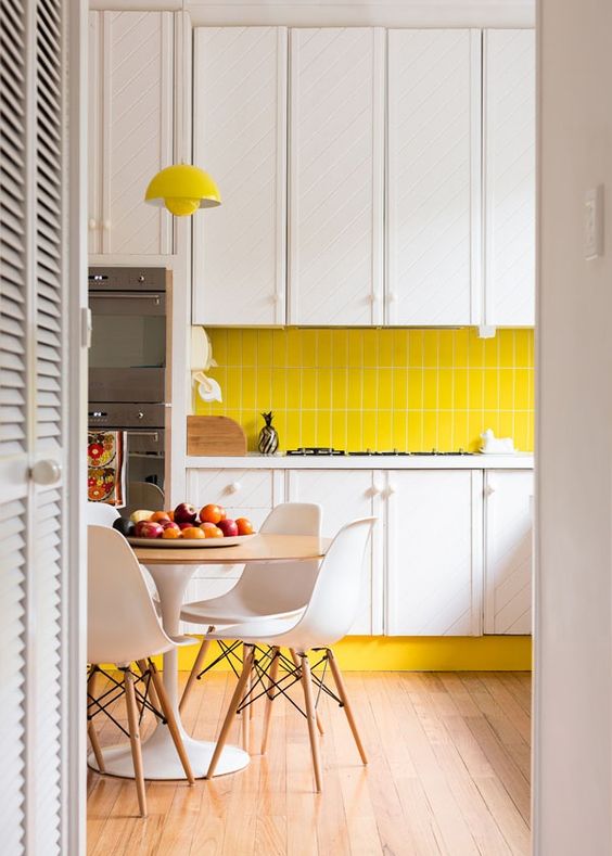 a contemporary kitchen with white cabinets, a bright yellow tile backsplash and a lamp, white chairs and neutrals
