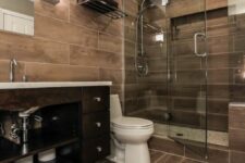 a cozy and cool bathroom completely clad with wood tiles, with a shower space, a dark vanity and a mirror plus built-in lights