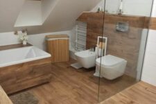 a cozy attic bathroom with wood tiles all over, a shower, a tub clad with wood, appliances and a wooden chest
