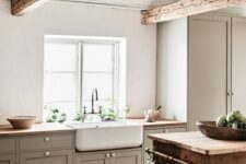 a cozy farmhouse neutral kitchen with grey cbainets, wooden countertops and beams, a wooden cart kitchen island