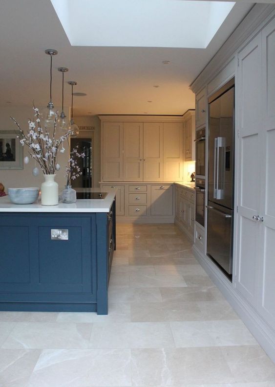 a dove grey kitchen with a bold blue kitchen island, white stone countertops and a neutral tile floor