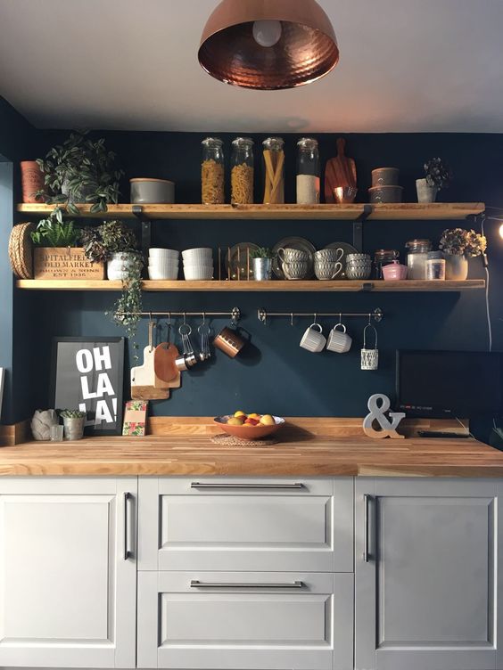a dove grey kitchen with a navy wall, wooden shelves and butcherblock countertops plus touches of copper and greenery