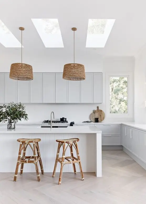 a dove grey kitchen with white countertops, a white backsplash, a white kitchen island, rattan stools and woven pendant lamps