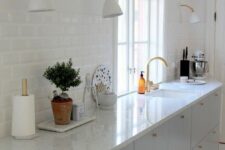 a dove grey kitchen with white stone countertops, a white tile backsplash, white sconces and gold touches