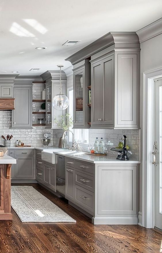 a farmhouse kitchen in dove grey with a white tile backsplash, a bubble lamp and rich stained wood for a warm touch