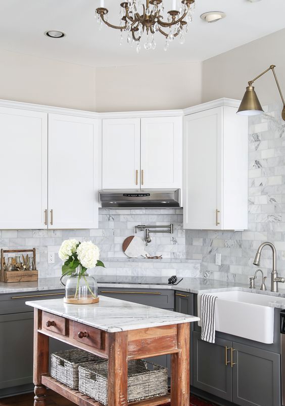a farmhouse kitchen with upper white cabinets, graphite grey ones, a marble tile backsplash and a stained kitchen island