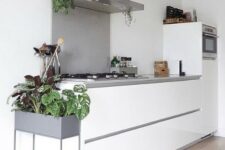 a minimal Nordic kitchen with sleek white cabinetry, a concrete countertop and backsplash, potted plants to refresh the space