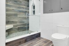 a minimal bathroom with wooden tiles and large scale white ones, a shower space, grey cabinets and white appliances