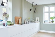 a minimalist kitchen with pale green walls, white sleek cabinets, black ceiling lamps looks fresh and natural
