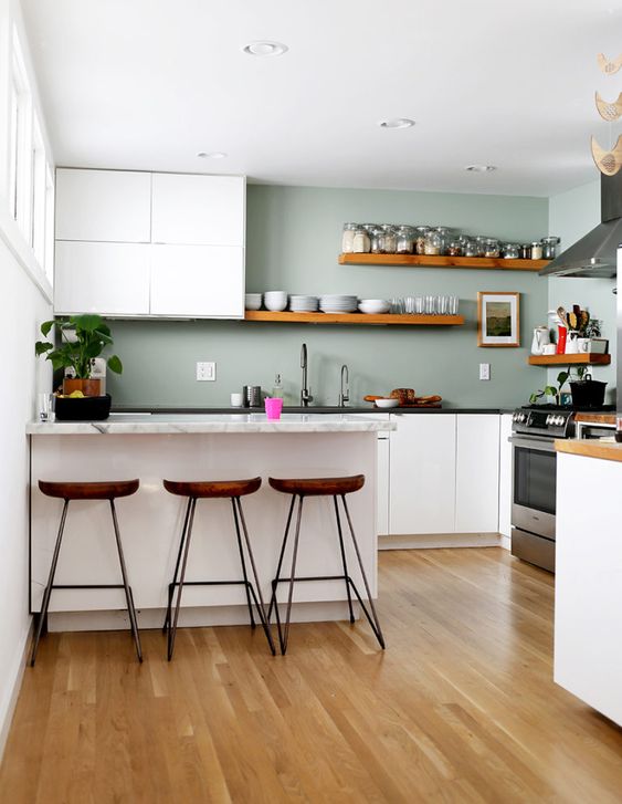 a minimalist kitchen with white cabinets, pale green walls, stone countertops and wooden shelves and stools