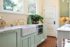 a mint farmhouse kitchen with shaker cabinets, white stone countertops, a bold printed rug and a vintage chandelier