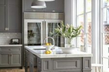 a modern farmhouse kitchen in grey with shaker style cabinets, a white subway tile backsplash, white marble countertops, grey pendant lamps