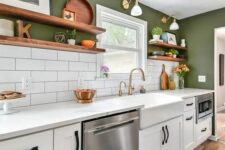 a modern farmhouse kitchen with green walls, white tiles, white cabinets and stone countertops, gold sconces