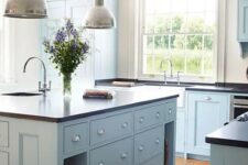 a modern light blue country kitchen with dark countertops, pendant lamps and large windows plus a lovely hardwood floor is chic