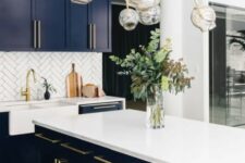 a navy kitchen with a white tile backsplash, white countertops and a statement gold and bubble chandelier