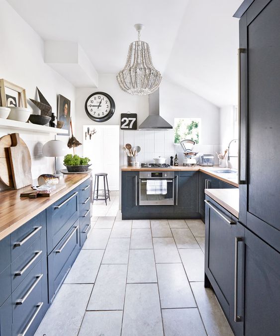 a navy kitchen with butcherblock countertops, a grey tile floor and a grey beaded chandelier for a bold touch