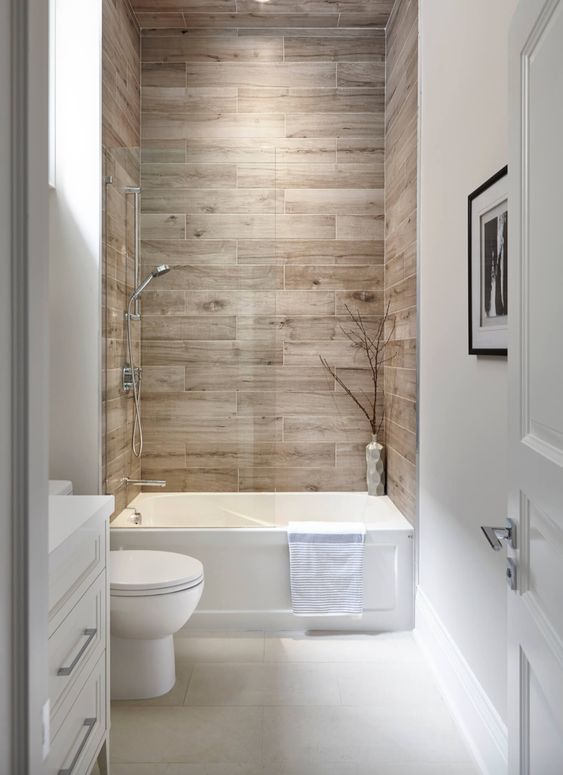 A neutral bathroom with wood tiles, a small tub, a toilet and a built in vanity is a cool and laconic space