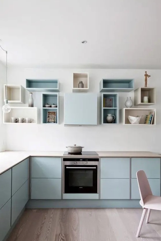 A pastel blue Scandinavian kitchen with sleek cabinets, box shelves on the wall and built in appliances