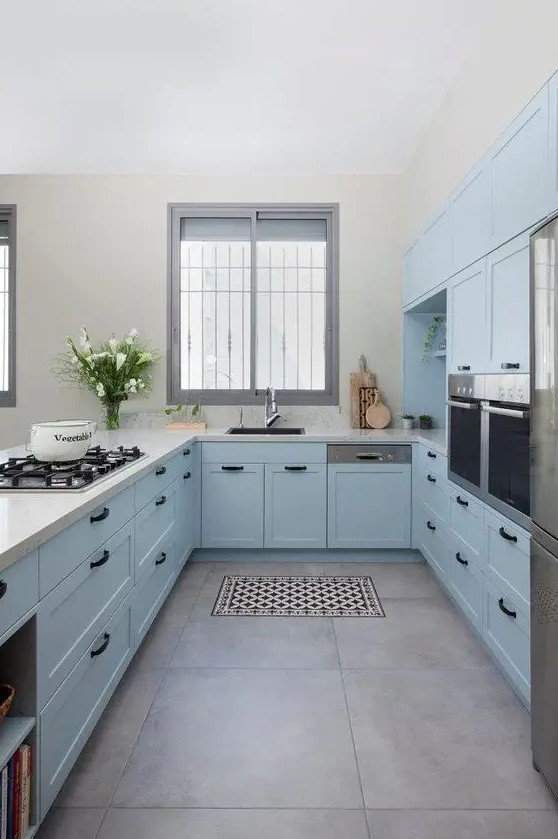 A pastel blue farmhouse kitchen with shaker cabinets, white stone countertops, black handles, built in appliances