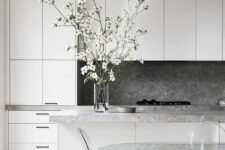 a refined minimalist kitchen done in white, with a grey stone backsplash and countertops, a glass table and acrylic chairs