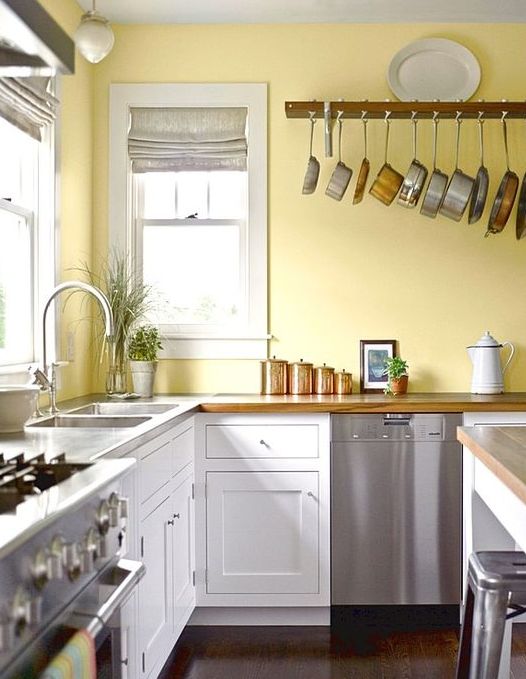 a retro kitchen with a lemon yellow wall, white cabinets, metal appliances and copper touches